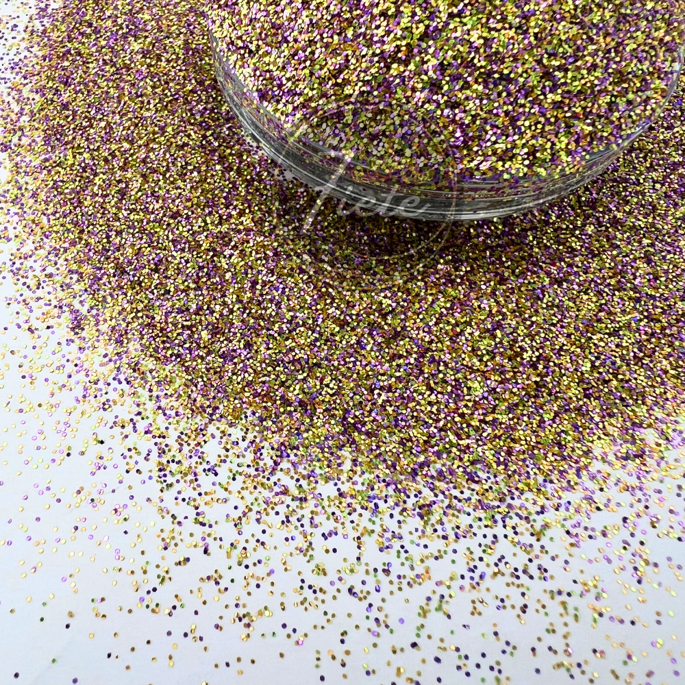 Close-up image of a custom glitter mix featuring shimmering purple, gold, and iridescent pieces scattered around a clear container, showcasing its high sparkle and colorful blend.