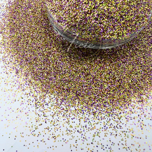 Close-up image of a custom glitter mix featuring shimmering purple, gold, and iridescent pieces scattered around a clear container, showcasing its high sparkle and colorful blend.