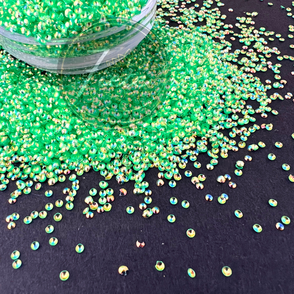 Bright neon green pearl glitter named Tianna displayed spilling from a clear container, featuring iridescent reflective highlights in gold, blue, and pink against a dark background.