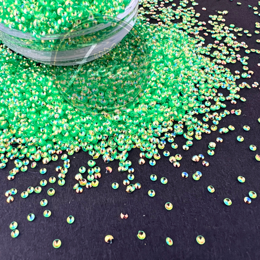 Bright neon green pearl glitter named Tianna displayed spilling from a clear container, featuring iridescent reflective highlights in gold, blue, and pink against a dark background.
