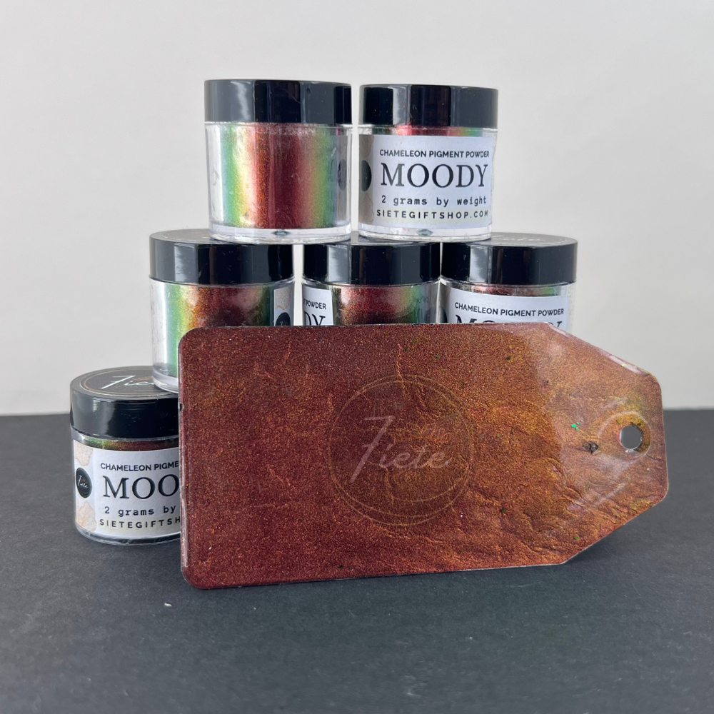 Chameleon pigment powder labeled “Moody” from Siete Gift Shop shown with multiple jars stacked and a green-to-gold color-shift sample tag displayed in front.