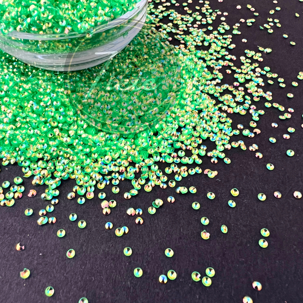 Bright neon green pearl glitter named Tianna displayed spilling from a clear container, featuring iridescent reflective highlights in gold, blue, and pink against a dark background.