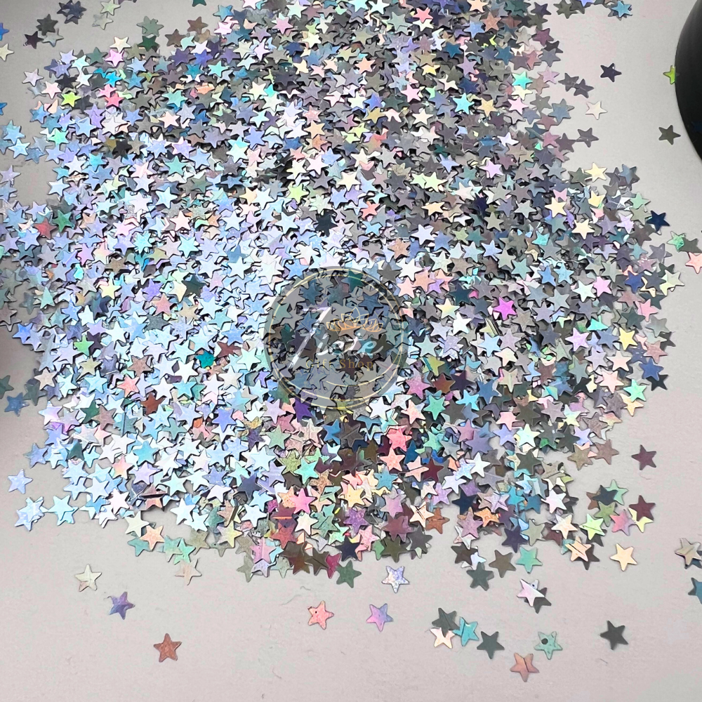 Silver holographic star-shaped glitter scattered on a light surface with rainbow reflective shine, Star – Silver Holographic Glitter by Siete Gift Shop