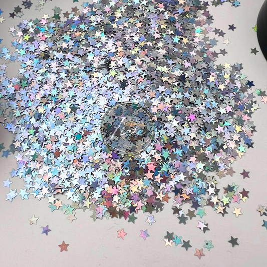 Silver holographic star-shaped glitter scattered on a light surface with rainbow reflective shine, Star – Silver Holographic Glitter by Siete Gift Shop