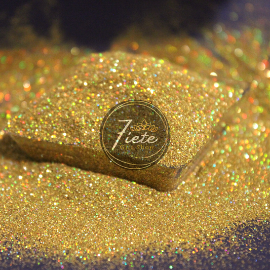 Extra fine glitter overflowing from a small clear container. The container is surrounded by the same glitters.  This glitter is holographic and gold, reflecting light showing all the colors of the rainbow. 