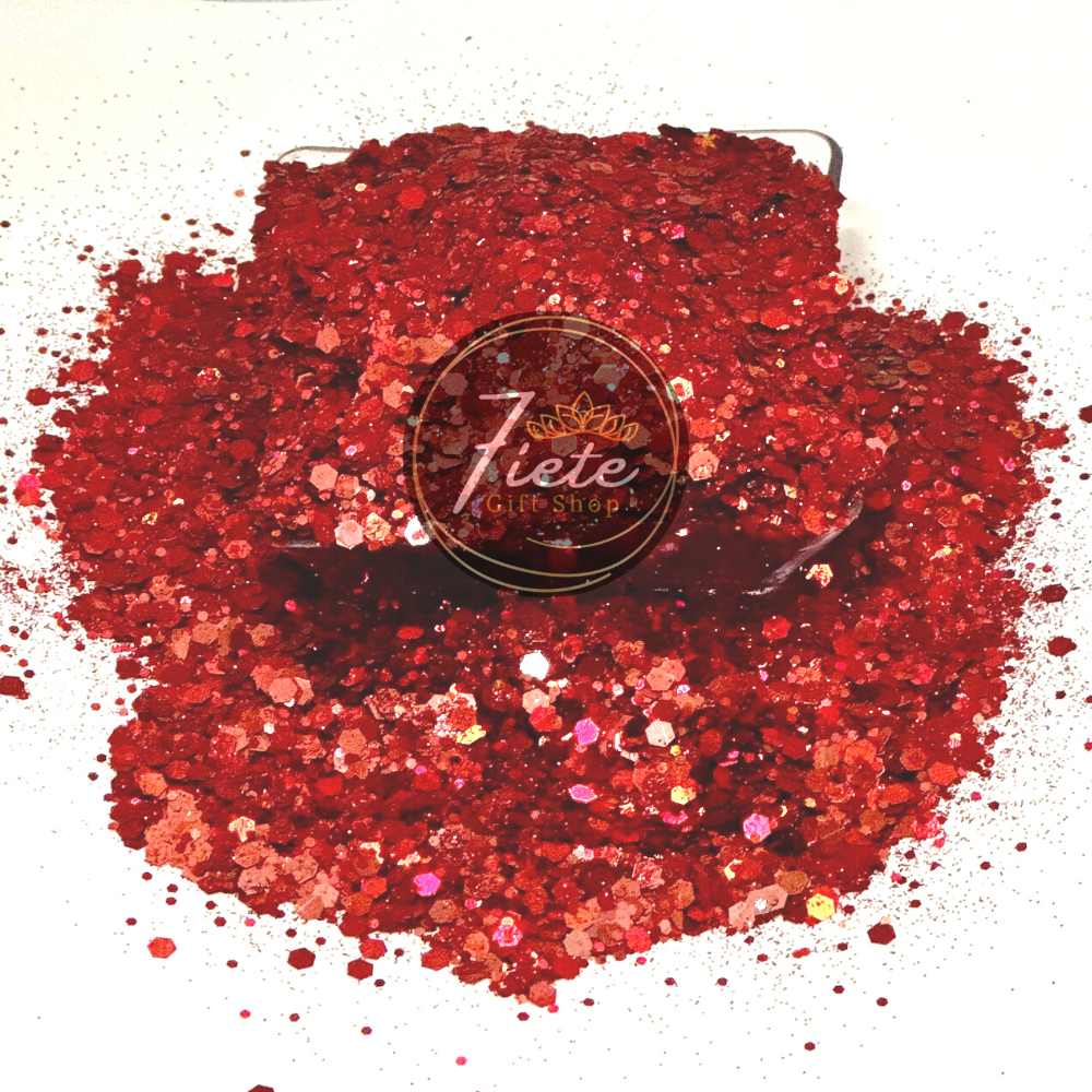 Red holographic chunky mix glitter over spilling from short clear container. The glitter is picking up different shades of reds, some subtle pinks and oranges.